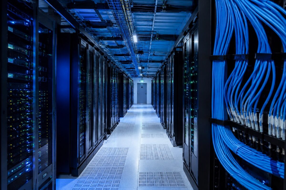 Corredor interno de um data center moderno com racks de servidores iluminados em azul e cabos de rede organizados.